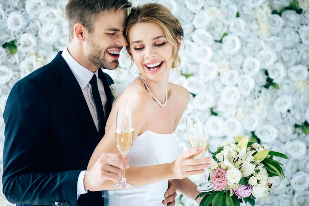 attractive bride and handsome bridegroom smiling and holding champagne glasses